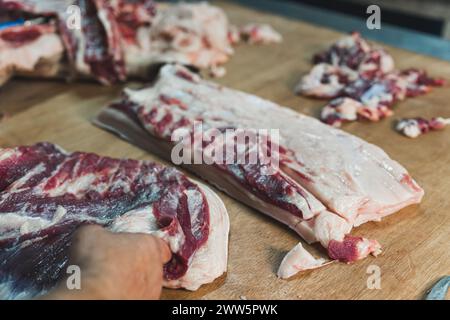 Nahaufnahme der Fleischverarbeitung in der Lebensmittelindustrie, der Arbeiter schneidet Rohschwein, Lagerung im Kühlschrank. Hochwertige Fotos Stockfoto