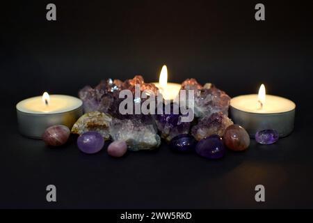 Wunderschöner lila Druzy mit Amethyst-Kristallen und brennenden Kerzen im Dunkeln. Selektiver Fokus. Stockfoto