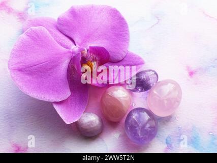 Amethyst-Kristalle, Rosenquarz und Orchideenblüte. Heilkristalle, die Magie der Edelsteine. Stockfoto