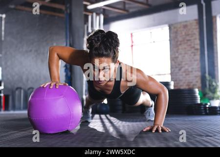Eine kräftige weiße Frau macht eine Plank auf einem violetten Trainingsball in einem Fitnessstudio Stockfoto