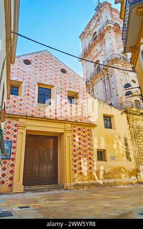 Die Fassade und der hohe Glockenturm der historischen Kirche San Juan von der engen Straße Calderon de la Barca in Malaga, Spanien Stockfoto