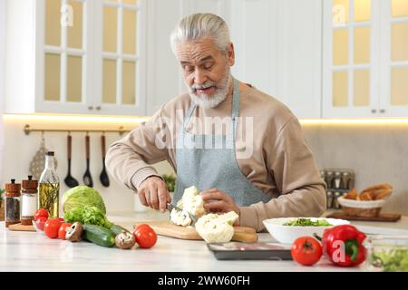 Glücklicher Mann, der Blumenkohl am Tisch in der Küche schneidet Stockfoto