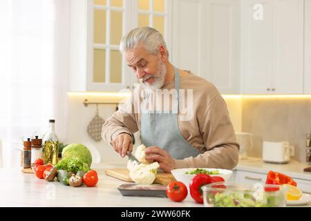 Glücklicher Mann, der Blumenkohl am Tisch in der Küche schneidet Stockfoto