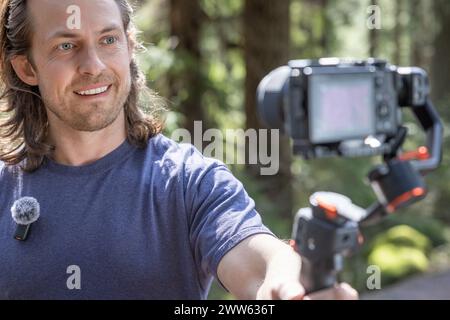 Content Creator verwendet ein Kamera-Gimbal, um in der Natur mit einem verschwommenen Wald im Hintergrund zu filmen Stockfoto