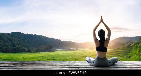 Asiatische Frau, die morgens auf dem Holzbalkon auf dem Reisfeld Yoga macht. Weibliches Glück. Querformat Stockfoto