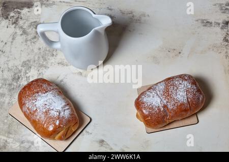 Hausgemachte Brötchen mit Marmelade mit Puderzucker auf hölzernem Hintergrund. Frische Bäckerei und Milchkännchen auf dem Küchentisch. Süßes Frühstück Stockfoto