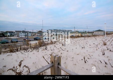 Strand an einem Wintertag, mit einer Reihe von Häusern entlang der Küste. Geparkte Fahrzeuge und ein Holzzaun verleihen der Szene einen Hauch von Leben. Der bewölkte Himmel und Stockfoto