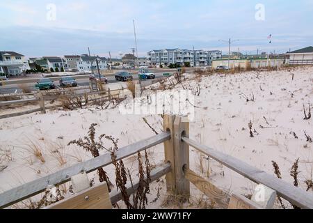 Eine ruhige Winterstrandszene mit Häusern an der Küste im Hintergrund, geparkten Fahrzeugen und einem Holzzaun, der den verschneiten Sand ziert. Ein ruhiger und friedlicher Mensch Stockfoto