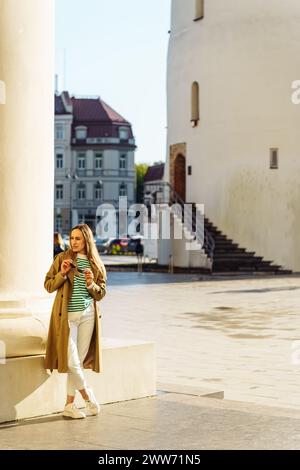 Eine attraktive junge Frau in lässiger Kleidung steht auf dem Platz der Stadt in der Nähe der Säule Stockfoto