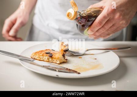 Person, die Ahornsirup auf hausgemachten Pfannkuchen gießt Stockfoto