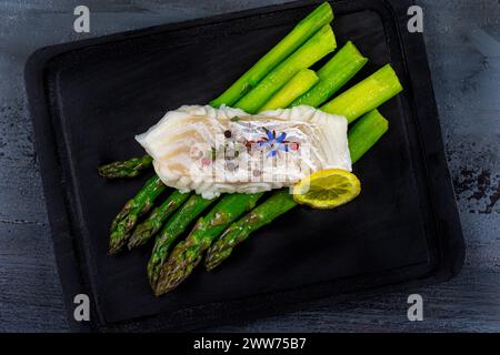 Kabeljausteak auf grünem Spargel auf einem schwarzen Brett. Stockfoto