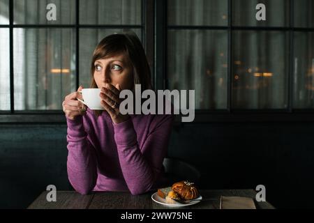 Frau trinkt Tee in einem Restaurant mit Kuchen auf einem Teller neben ihr Stockfoto