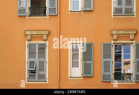 Frankreich. Cannes. Wunderschöne Holzfenster mit Rollläden. Wunderschöne Holzfenstern mit Fensterbank, orangefarbene Zementwand an einem sonnigen Tag Stockfoto