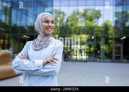 Porträt einer positiven, erfolgreichen muslimischen Geschäftsfrau in einem Hijab, die selbstbewusst in einer städtischen Umgebung lächelt. Stockfoto