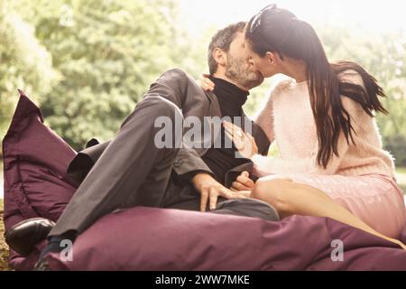 Paar, sitzen auf großen Kissen im Park küssen Stockfoto