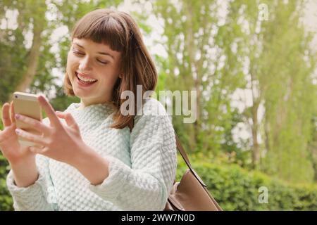 Lächelndes Teenager-Mädchen, Das Draußen Ein Smartphone Benutzt Stockfoto