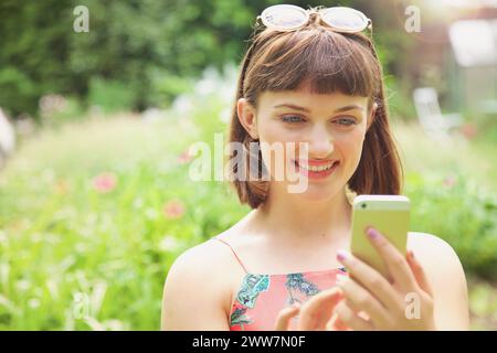 Nahaufnahme eines lächelnden Teenager-Mädchens, das draußen ein Smartphone benutzt Stockfoto