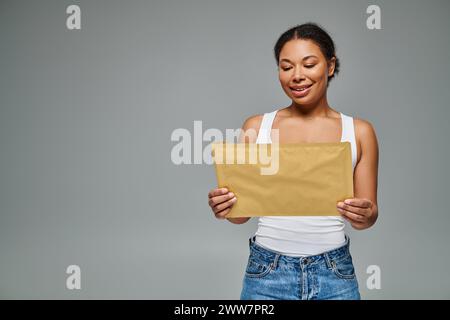 Glücklicher afroamerikaner, der einen Umschlag mit einem Diätplan vor grauem Hintergrund hält Stockfoto