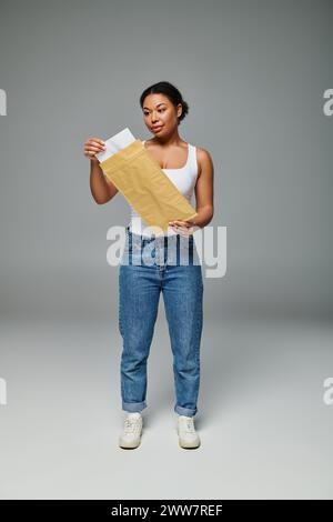 Glückliche afroamerikanerin, die einen Umschlag mit einem Diätplan auf grauem Hintergrund hält Stockfoto