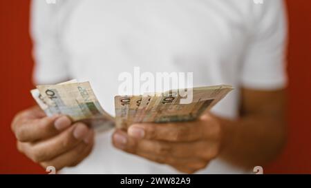 Ein junger hispanischer Mann zählt polnische Zloty-Währung, isoliert gegen eine rote Mauer. Stockfoto