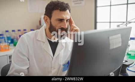 Konzentrierter Mann mit Bart, der Laborkittel trägt und Daten am Computer im Forschungslabor analysiert Stockfoto