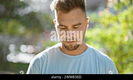 Ein besinnlicher hispanischer Mann mit Bart posiert im Freien, umgeben von Grün in einem ruhigen Stadtpark. Stockfoto