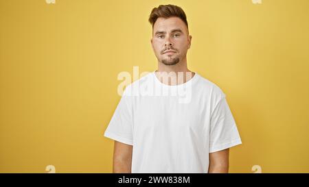 Ein junger hispanischer Mann mit Bart posiert vor einem gelben Hintergrund und trägt ein weißes T-Shirt. Stockfoto