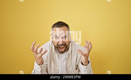 Ein reifer Mann mit grauem Bart schreit vor einem isolierten gelben Hintergrund. Stockfoto