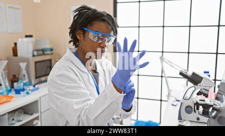 Eine junge afroamerikanische Wissenschaftlerin mit Labormantel und Schutzbrille bereitet sich auf ein Experiment in einem Labor vor. Stockfoto