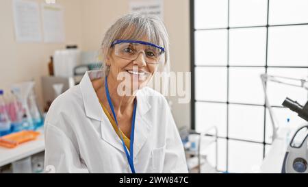 Lächelnde reife Wissenschaftlerin mit grauem Haar in einem Labor mit Schutzbrille Stockfoto