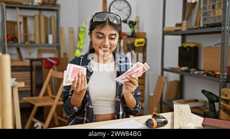 Eine junge indianerin lächelt, während sie isländische Krone in einer gut organisierten Tischlerei hält. Stockfoto