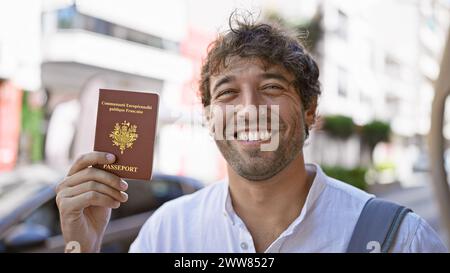 Hübscher bärtiger Mann mit grünen Augen, der einen französischen Pass auf einer sonnigen Straße hält. Stockfoto