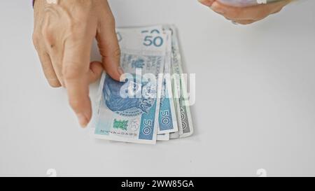 Eine reife Frau zählt polnische Zloty-Banknoten vor weißem Hintergrund, was auf Finanzmanagement und Sparguthaben hinweist. Stockfoto
