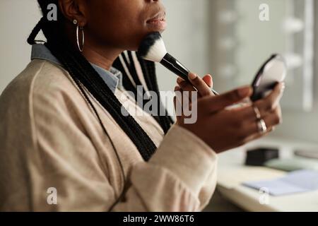 Nahaufnahme der schwarzen jungen Frau, die am Kosmetiktisch Make-up macht und den Kopierraum für Gesichtspuder aufsetzt Stockfoto