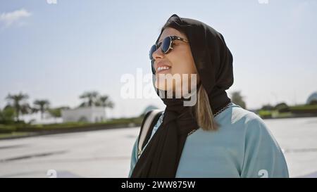 Eine lächelnde junge Erwachsene hispanische Frau, die einen Hijab in einer islamischen Moschee in abu dhabi, vae, trägt. Stockfoto