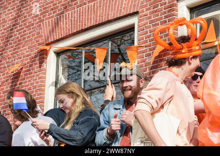 Lächelnde Menschen mit niederländischer Flagge im Gesicht und in orangefarbener Kleidung zum Königstag - Niederlande, Amsterdam, 27.04.2023 Stockfoto