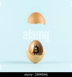 Goldenes Ei mit einem Bitcoin-Zeichen in gebrochener Eierschale auf pastellblauem Hintergrund. Minimales Investitionskonzept. Stockfoto