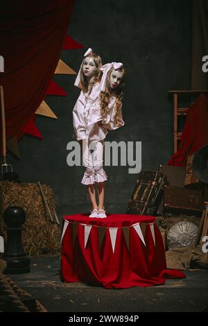 Siamesische Zwillingsmädchen in weißen Vintage-Kostümen mit Make-up über dunklem Retro-Zirkus Hintergrund. Kreatives, gruseliges Spiel Stockfoto