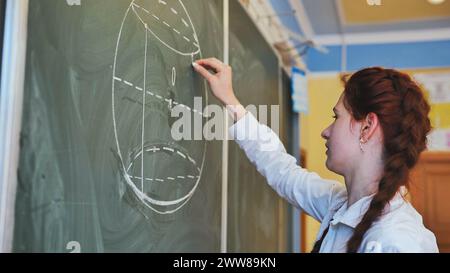 Ein rothaariges Schulmädchen zeichnet geometrische Formen auf dem Spielbrett. Stockfoto