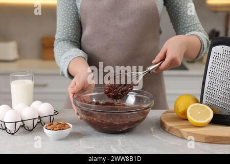 Frau mischt Schokoladencreme mit Schneebesen in einer Schüssel an einem grauen Marmortisch drinnen, Nahaufnahme Stockfoto