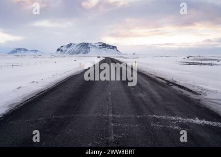 Leere Straße im Winter in Island, die während des Sonnenaufgangs mit Schnee bedeckt ist Stockfoto