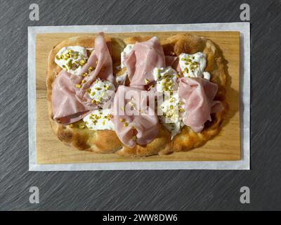 Römische Pinsa, Variante der klassischen italienischen Pizza, garniert mit Mortadella, Stracciatella, Lammsalat und Pistazien Stockfoto