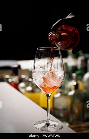 Der Barkeeper, der den Aperol Spritz Cocktail zubereitet, gießt Champagner in das Glas mit Eis. Stockfoto