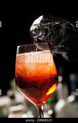 Der Barkeeper, der den Aperol Spritz Cocktail zubereitet, gießt Wasser in das Glas mit Eis. Stockfoto