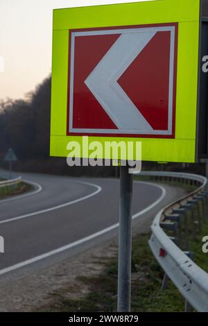 Asphaltstraße mit hellen Verkehrsschildern vor der scharfen Linkskurve. Stockfoto
