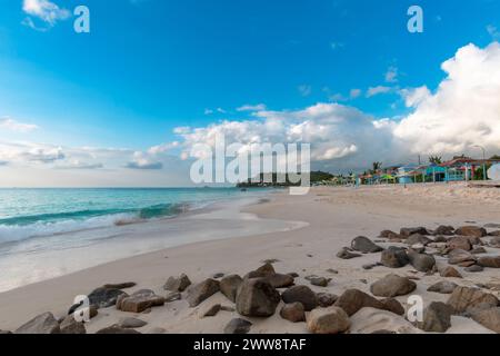 Ruhige Wellen, die an einem weißen Sandstrand auf der tropischen Insel Antigua mit Felsen im Vordergrund und klarem blauem Wasser auftauchen Stockfoto