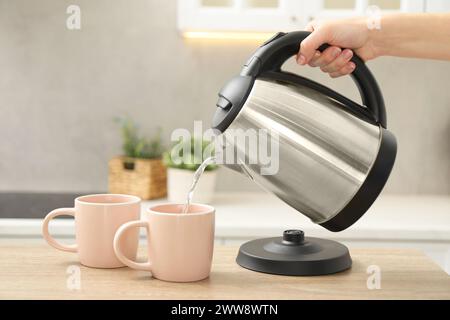 Frau, die heißes Wasser aus dem Wasserkocher in die Tasse in der Küche gießt, Nahaufnahme Stockfoto