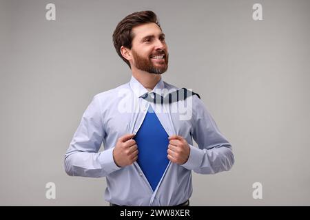 Glücklicher Geschäftsmann, der ein Superheldenkostüm unter dem Anzug auf beigefarbenem Hintergrund trägt Stockfoto