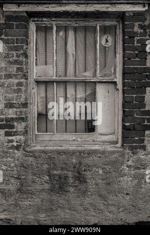 Stimmungsvolle alte alte, verfallene rote Backsteinschuppen-Fenster mit abblätternder Farbe und Metallstäben. Dorset Coast. Historisch. Gruselig. Grungy. Schwarzweiß. Stockfoto