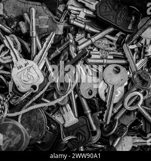 Nahaufnahme eines Tabletts mit alten Autoschlüsseln, Hausschlüsseln und antiken Schlüsseln. Glänzendes Metall, rostiges Metall. Konzept - Schlösser, Sicherheit, Türen. Schwarzweiß Stockfoto